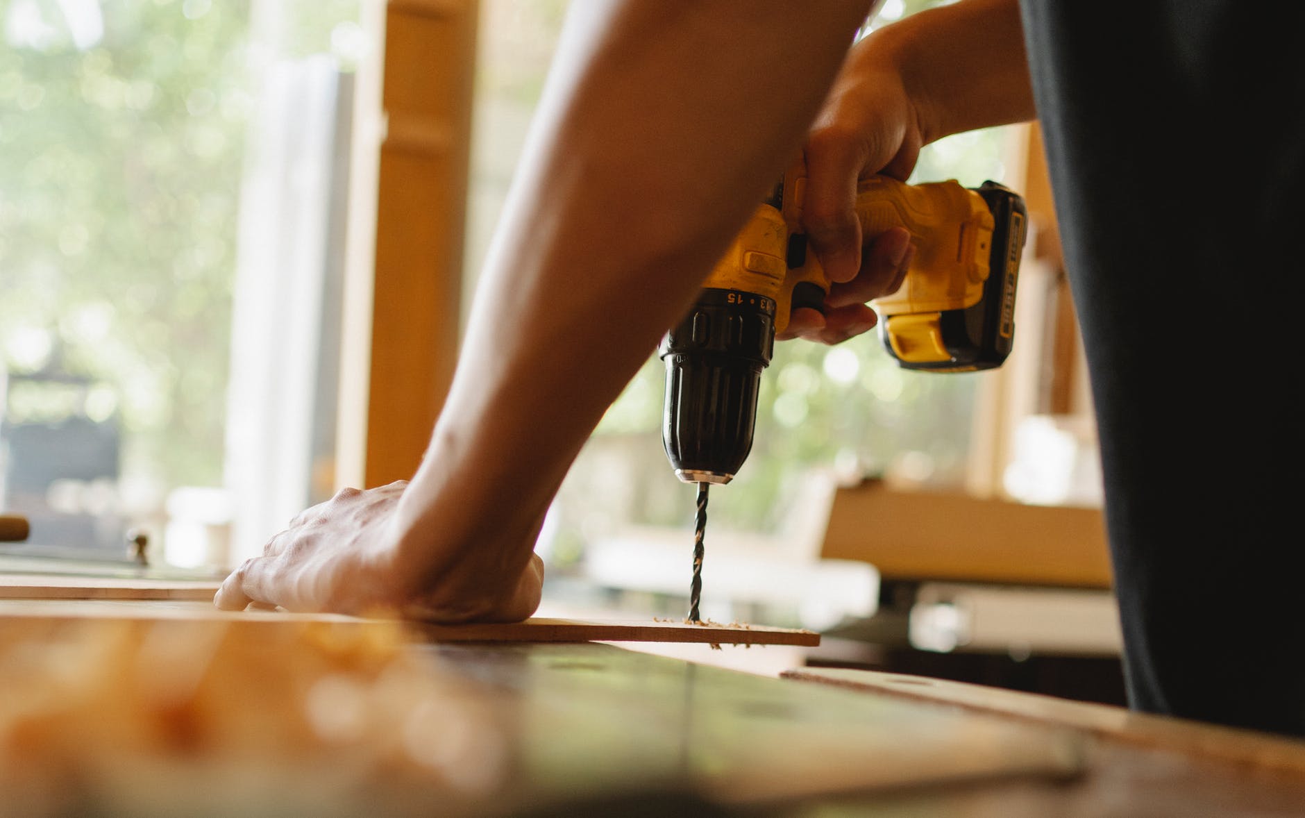 man drilling wooden plank on desk